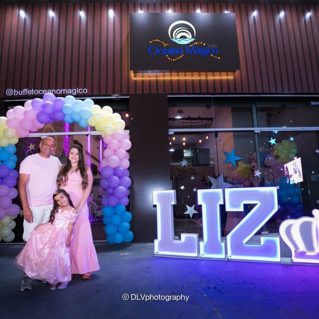 Família na entrada do Buffet Oceano Mágico com letreiro iluminado personalizado, Guarujá